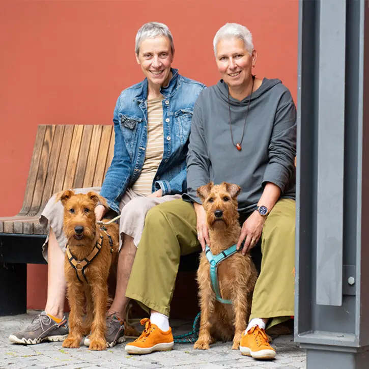 Susanne Hengehold-Schmidt | Heilpraktikerin Winsen Luhe. Auf dem Bild zu sehen, Susanne und Ihre Frau auf einer Bank mit den gemeinsamen Hunden.